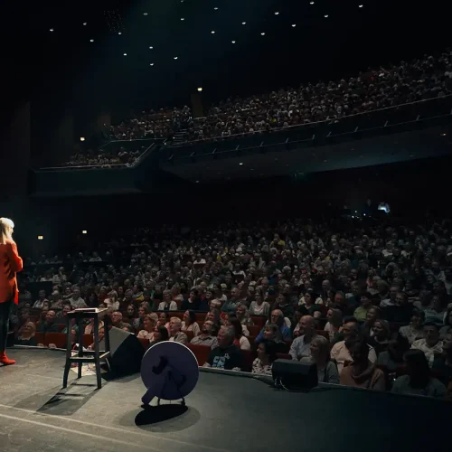 Komikerin Mirja Regensburg klein auf der Bühne mit Blick in den vollbesetzten Theatersaal beim emotionalen Tourabschluss in Kassel.