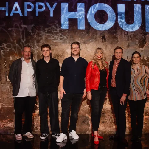 Komikerin Mirja Regensburg in roter Lederjacke steht mit der Gästerunde vor der „Happy Hour“-Graffiti-Wand der 3sat-Show in Berlin.