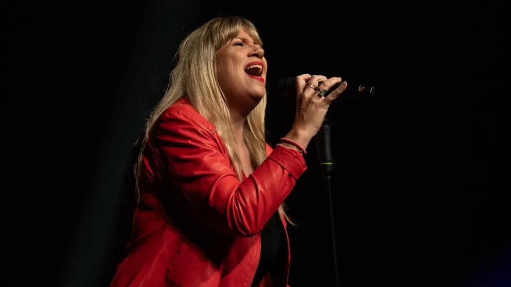 Mirja Regensburg in roter Lederjacke singt mit geschlossenen Augen in ein Mikrofon am Ständer