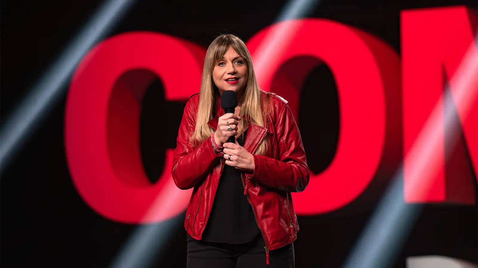 Mirja Regensburg moderiert auf der großen Bühne im Palladium Köln vor dem leuchtenden Schriftzug Die besten Comedians Deutschlands