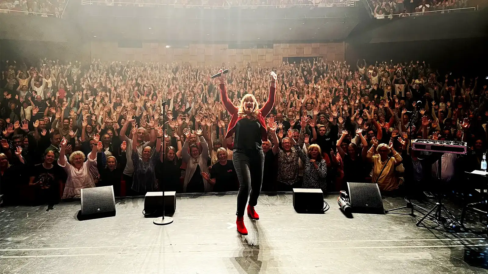 Mirja Regensburg feiert mit erhobenen Armen auf der Bühne vor einem ausverkauften, winkenden Publikum