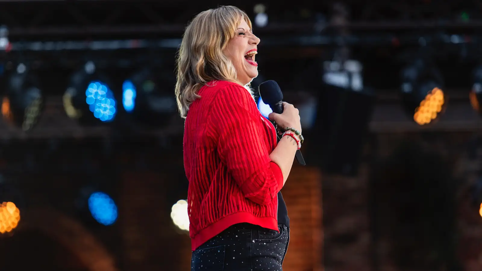 Mirja im roten Cardigan lacht mit Mikrofon in der Hand auf der Bühne des ZDF Comedy Sommer